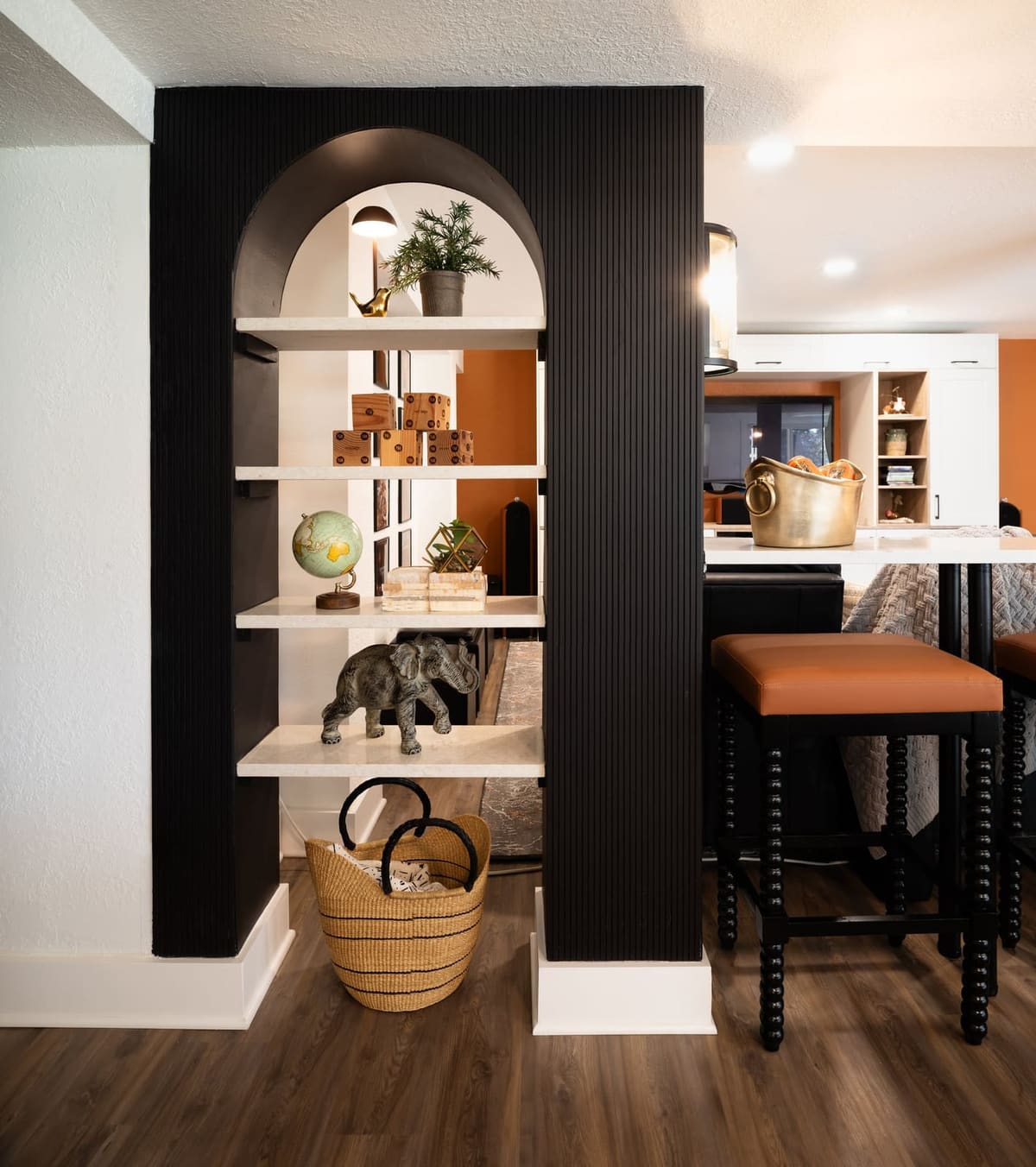 Basement bar with a black fluted arched shelf divider, stone shelves and cognac leather counter stools