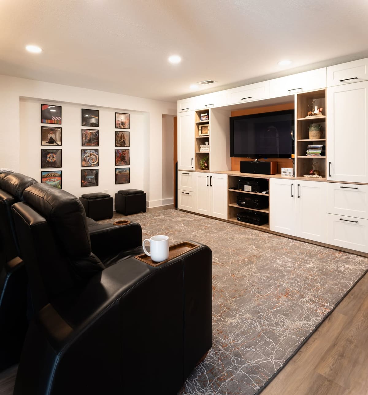Basement media room with black leather theater seats, a white shaker media wall and framed album cover art