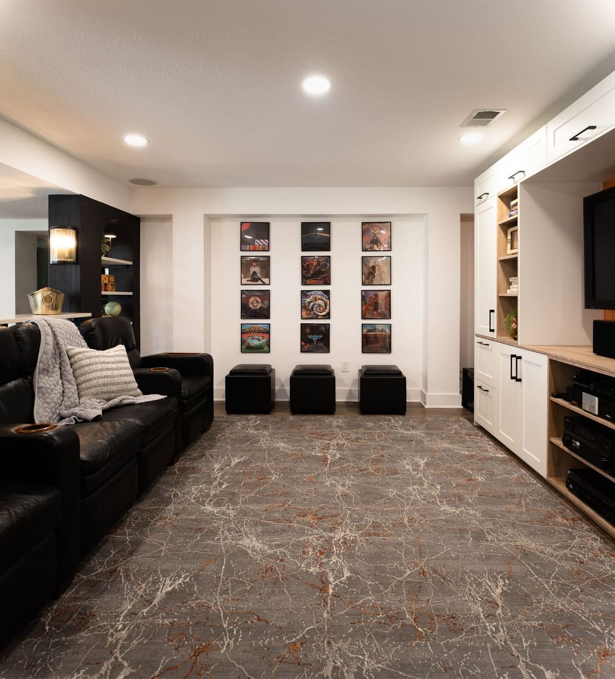Long view of a basement media room with black theater recliners, album art wall and white built-ins