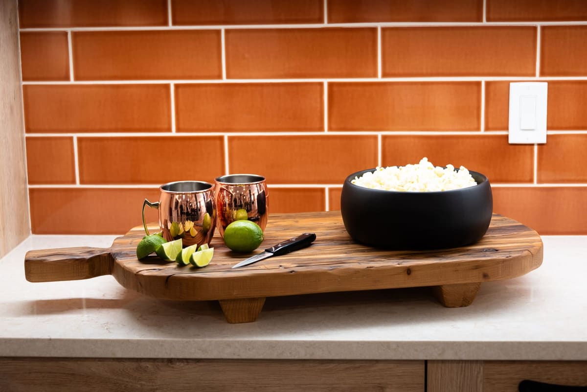 Reclaimed wood serving board with copper mugs, limes and popcorn against orange glazed subway tile