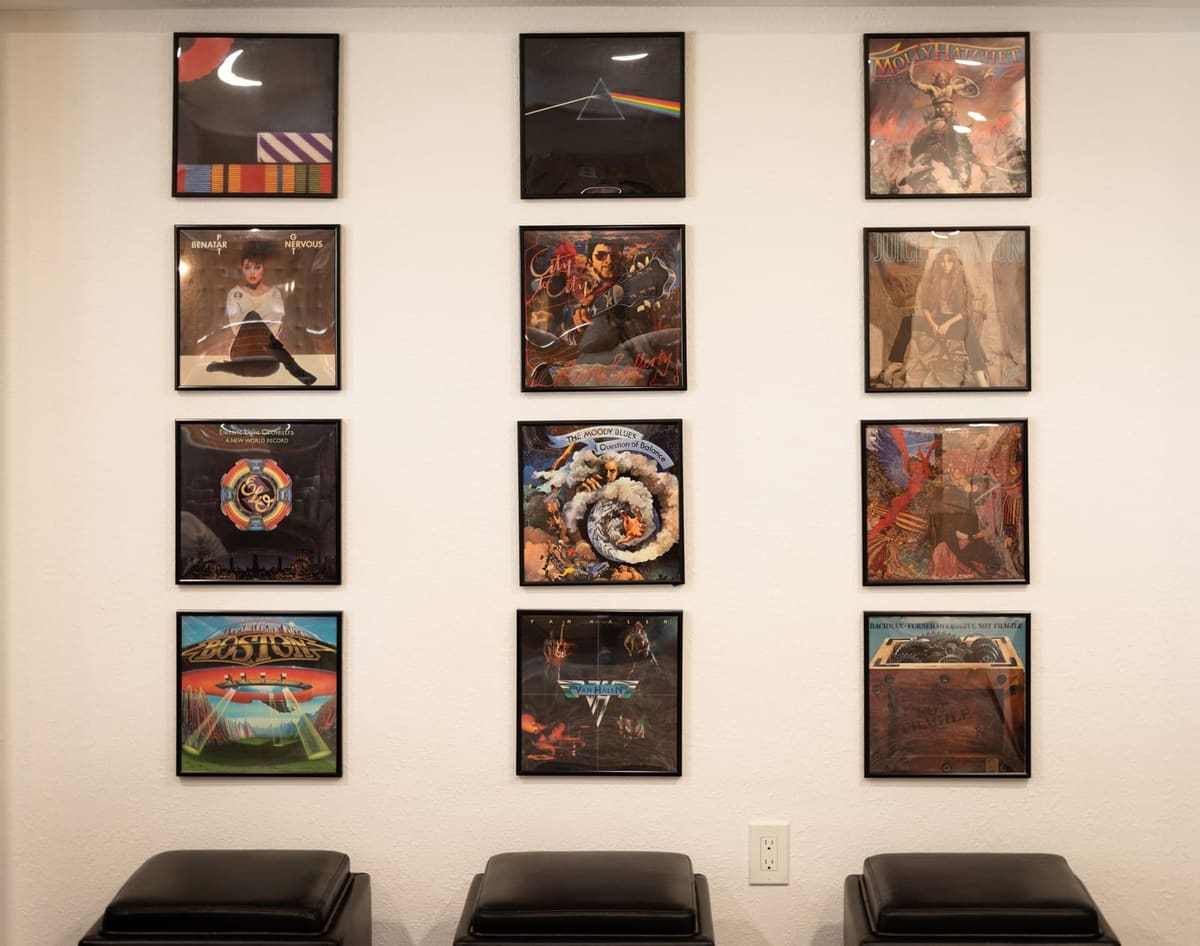 Grid of twelve framed vinyl album covers above three black leather storage ottomans in a basement media room