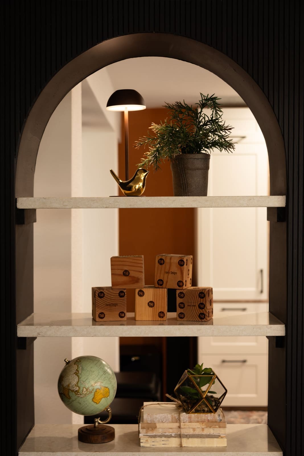 Arched black shelf niche styled with wood blocks, a globe and a brass bird lamp in a finished basement