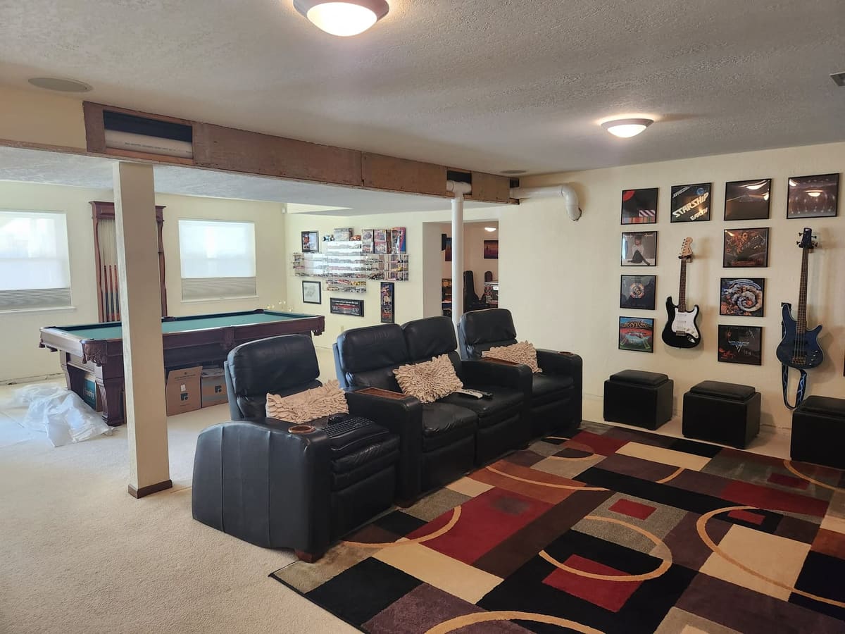 Before the remodel: carpeted basement with an open soffit and exposed pipes, pool table and theater seating