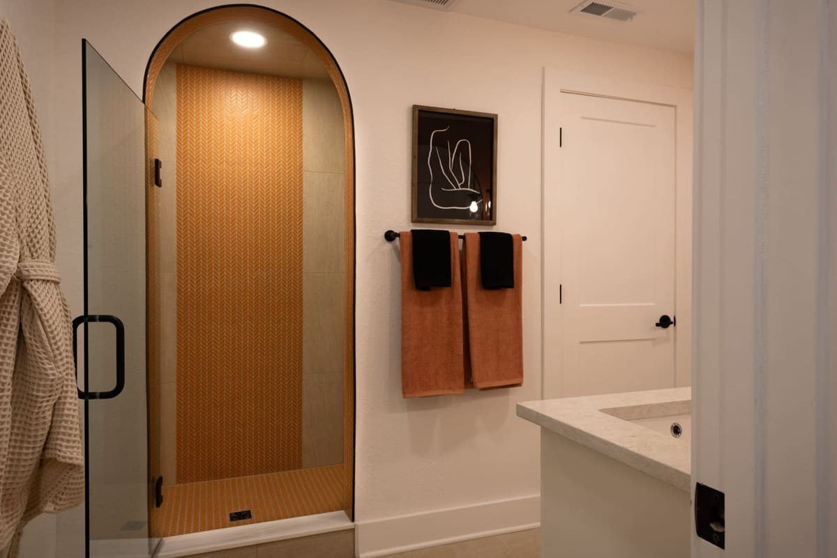Arched shower opening in orange chevron tile beside towel hooks and a white vanity