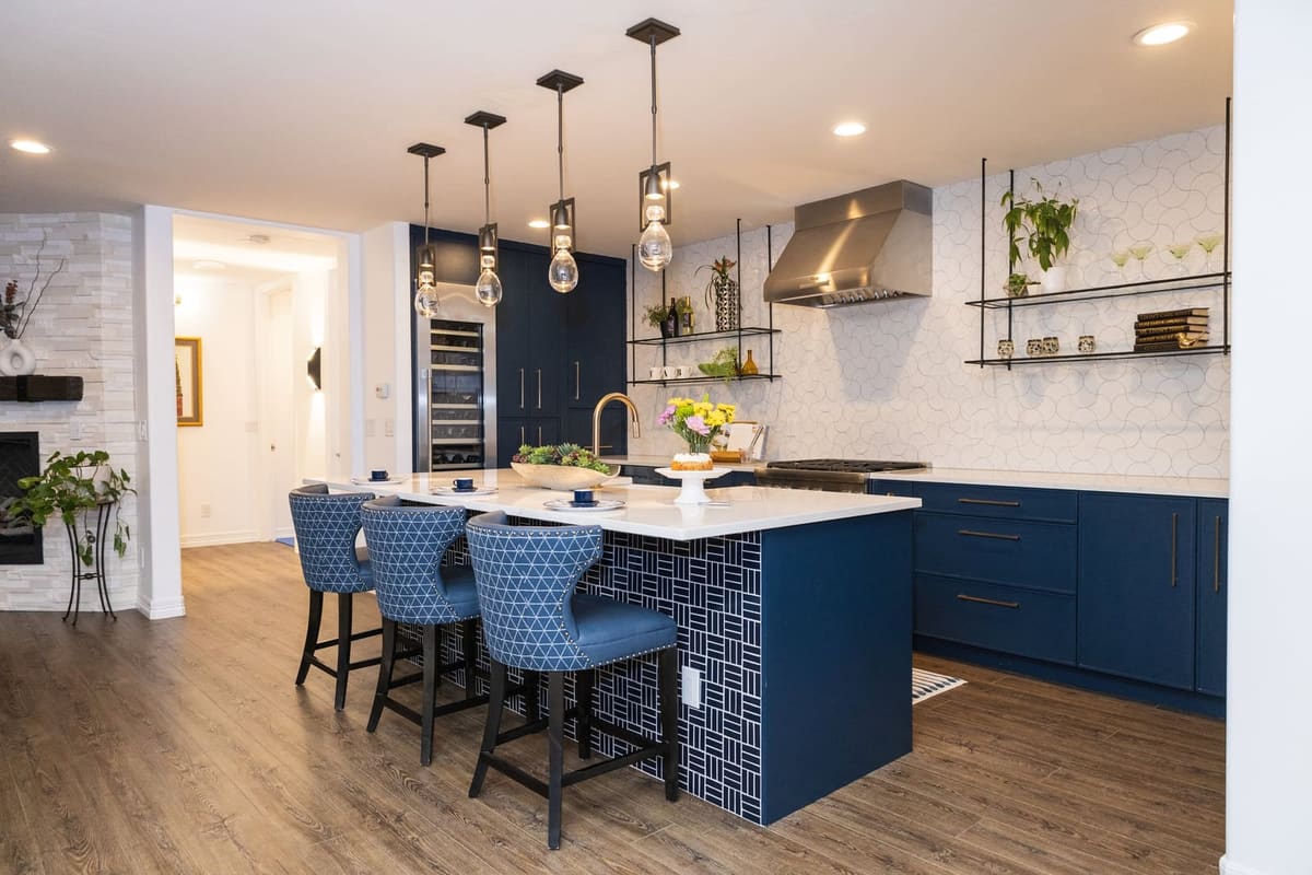 Navy kitchen island with blue upholstered stools and a white hexagon tile wall with hanging shelves