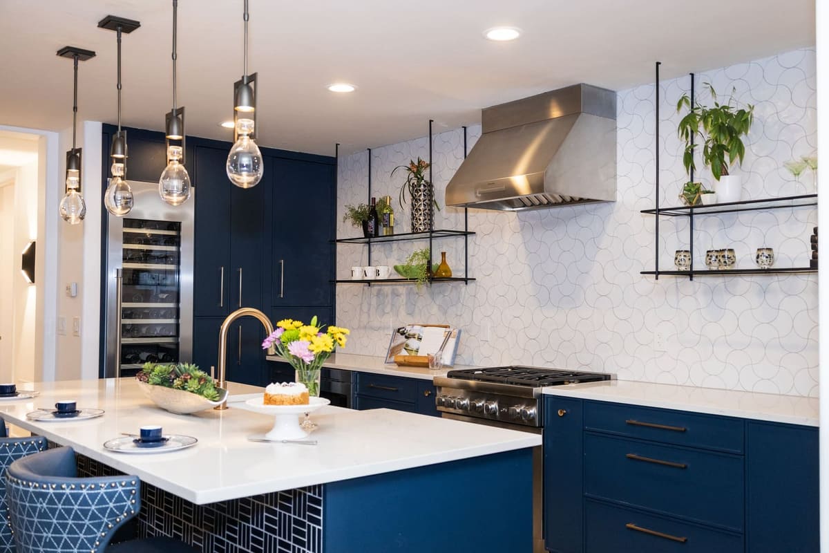 Island with a navy pattern-tiled base under glass pendants, a stainless hood on white hex tile