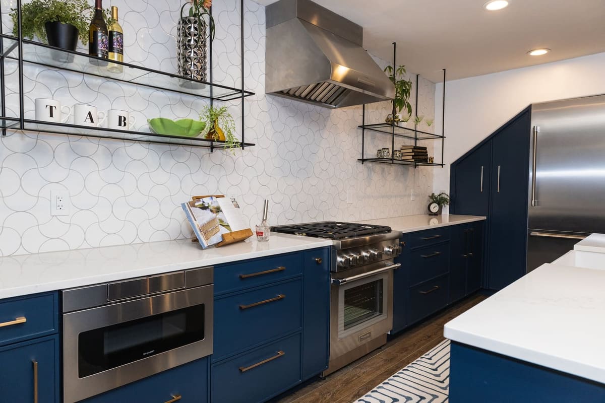 Navy cabinets with a pro range and microwave drawer under hanging metal shelves and white hex tile