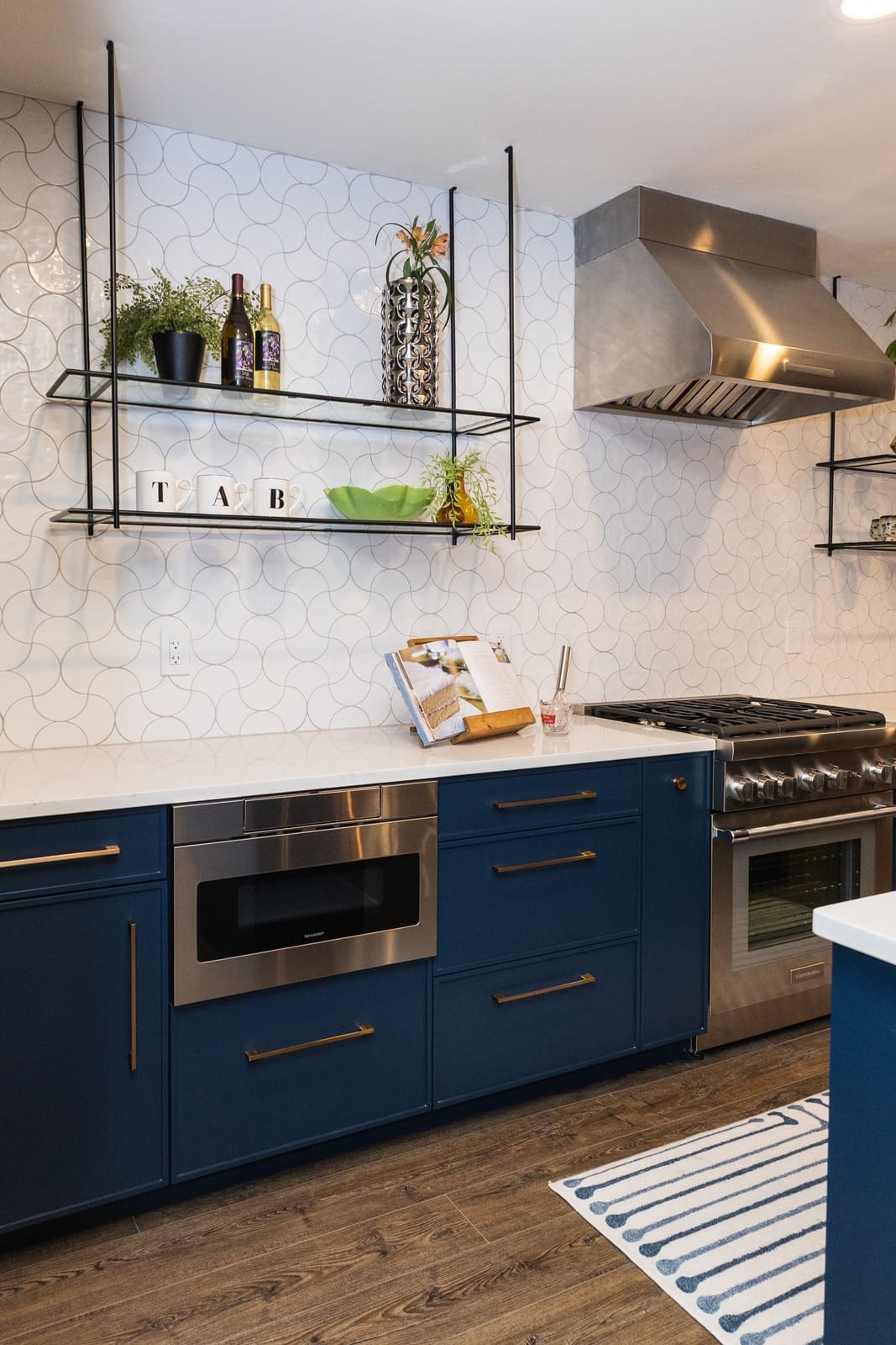 Navy cabinets and hanging glass shelves against white hexagon tile