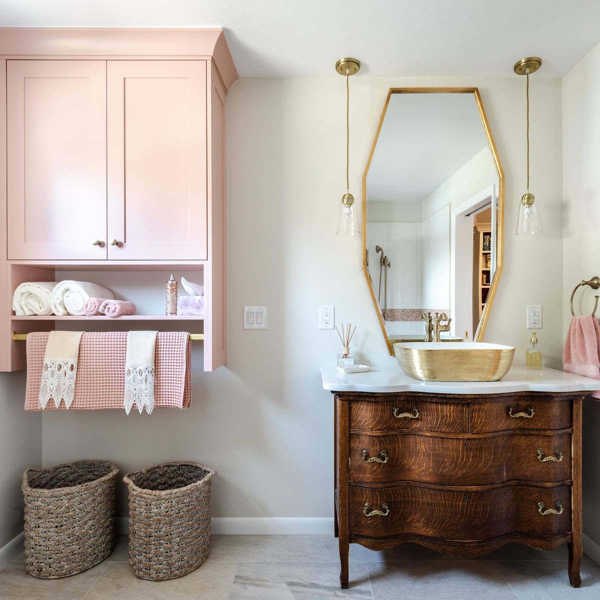 Pink wall cabinet over an antique dresser vanity with a gold vessel sink and hexagon gold mirror