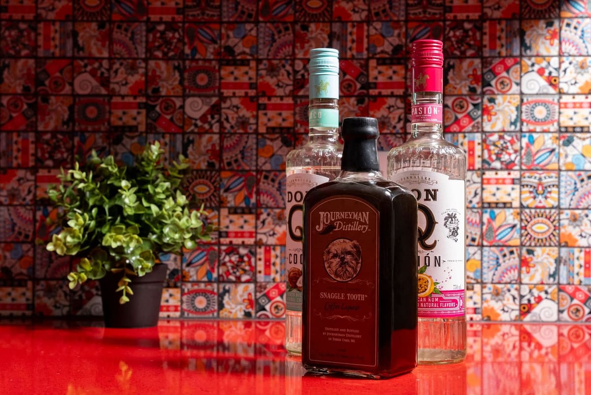 Liquor bottles and a potted plant on a glossy red quartz counter against multicolor patterned tile