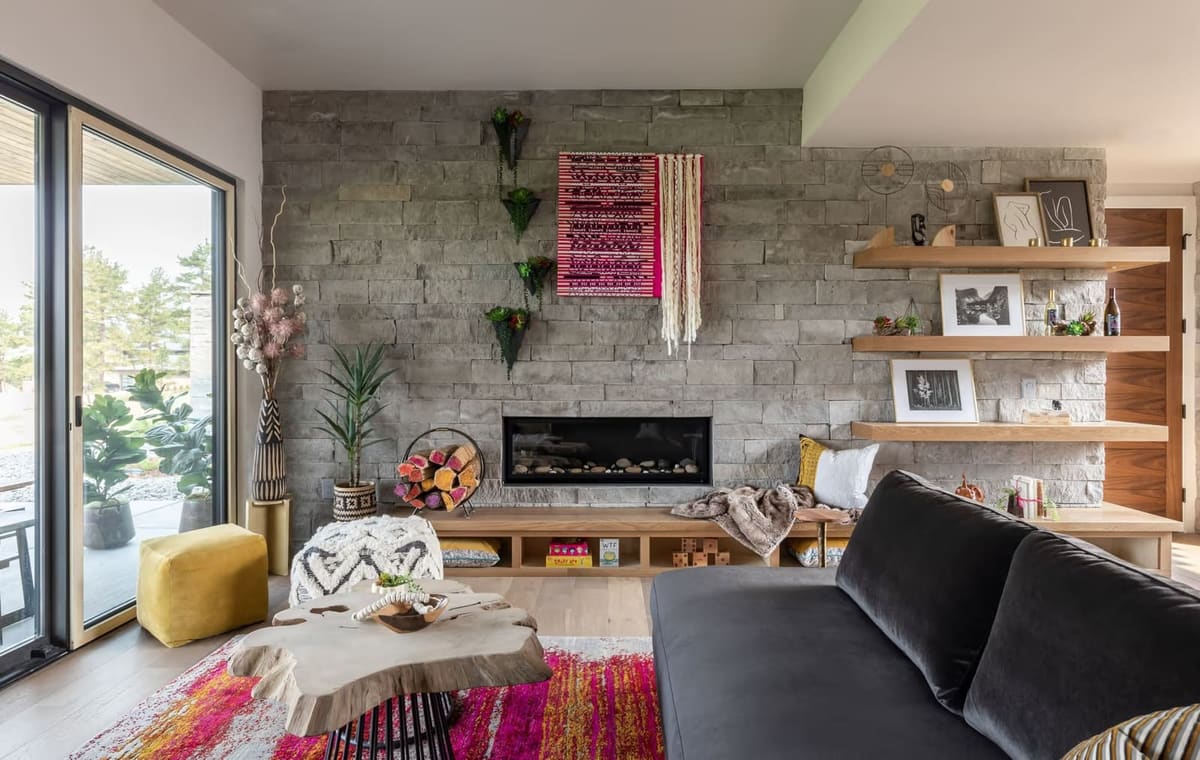 Gray stacked stone wall with linear fireplace, pink woven wall hanging, white oak floating shelves and built-in bench