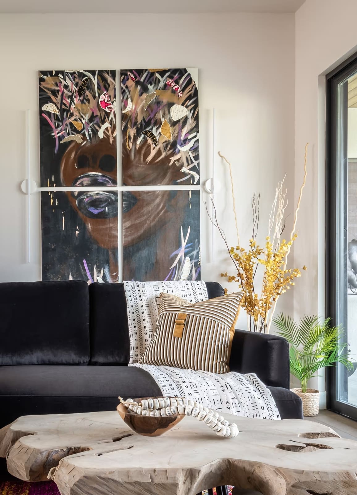 Black velvet sofa with mudcloth throw and striped pillow, live-edge wood coffee table and large four-panel portrait art
