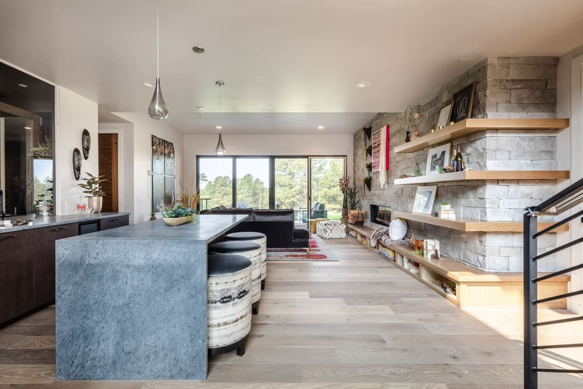 Gray stone waterfall island next to a long stacked stone wall with oak floating shelves and a low built-in bench