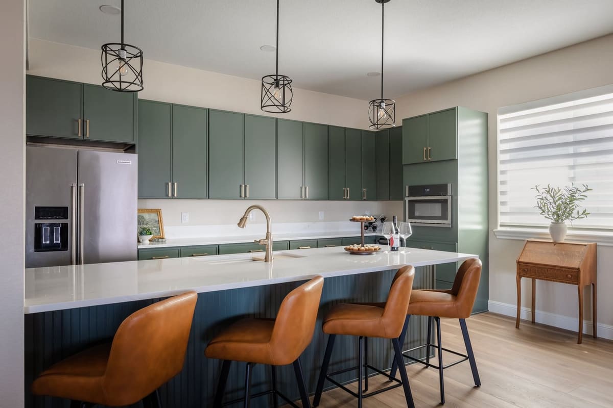 White quartz island with cognac leather stools facing sage cabinetry and a stainless refrigerator