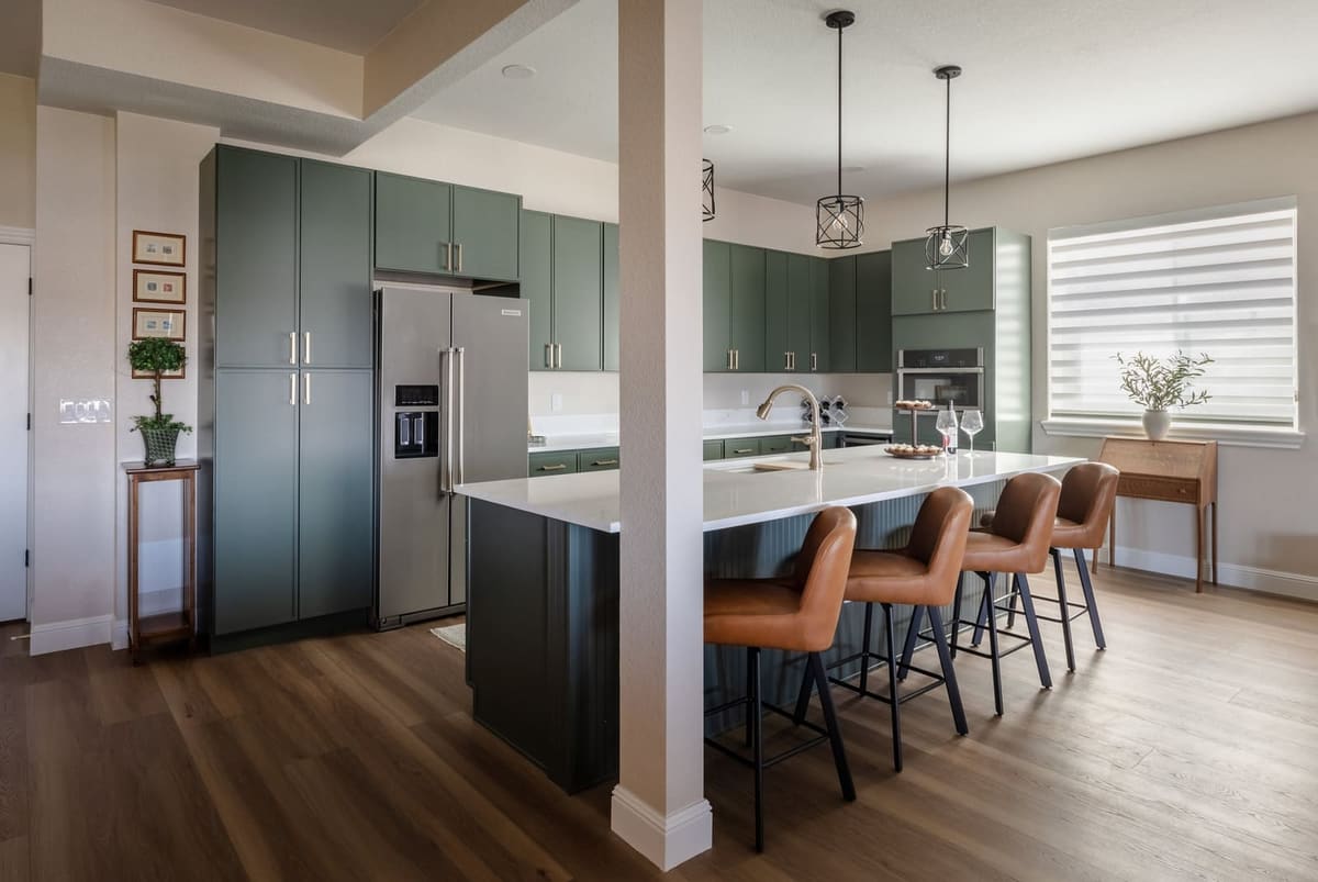 Sage kitchen seen past a column, cognac stools at the island and full-height sage pantry cabinets