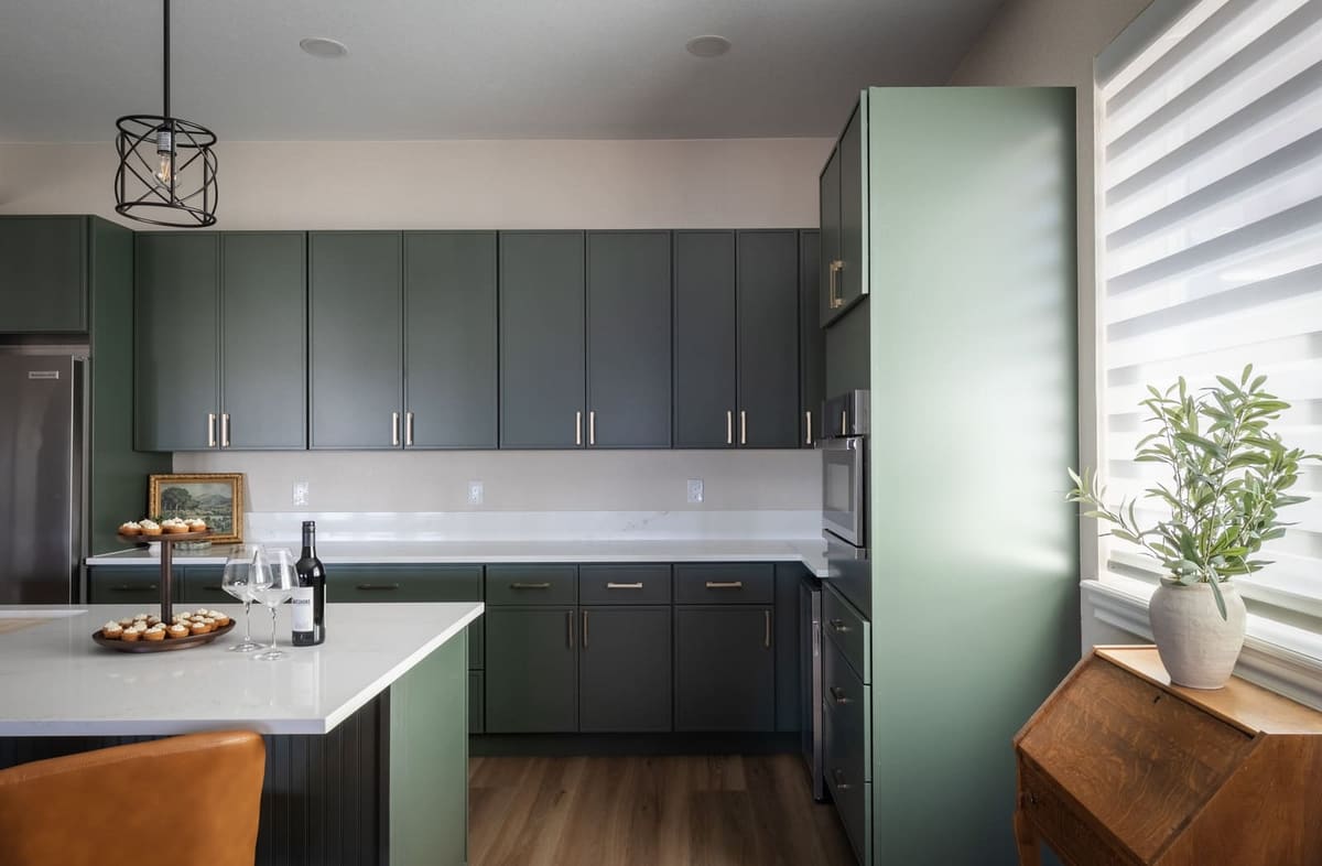 Sage green cabinets and white quartz beside a tall sage pantry and a potted olive tree