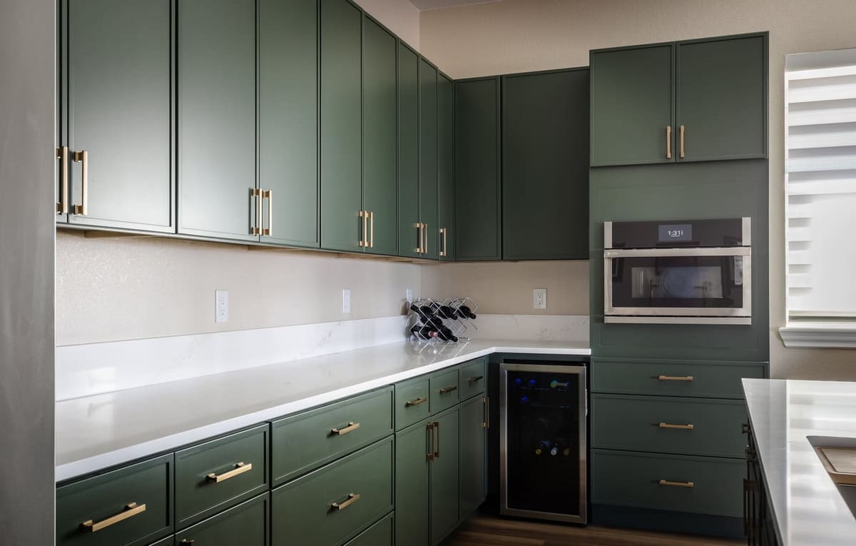 Sage cabinet wall with brass pulls, a built-in microwave and wall oven and a wine fridge