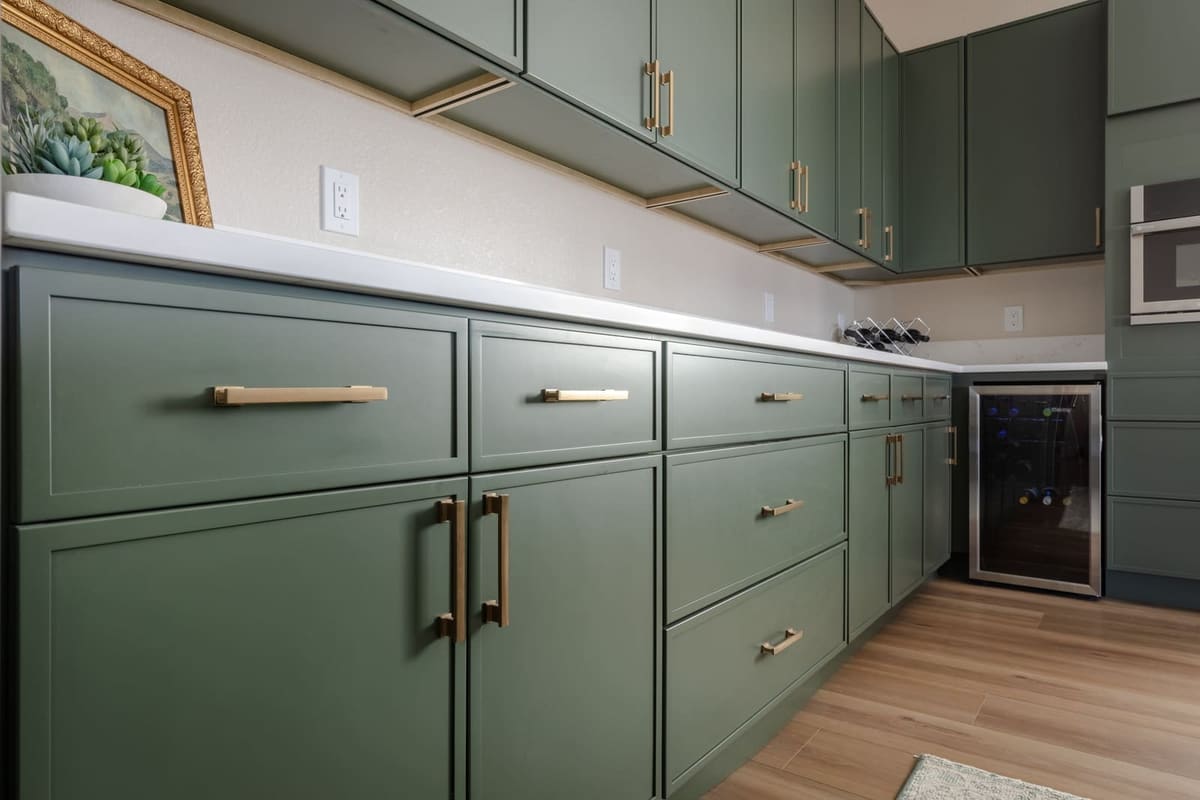 Sage green lower cabinets with brushed brass pulls and a wine fridge under white quartz