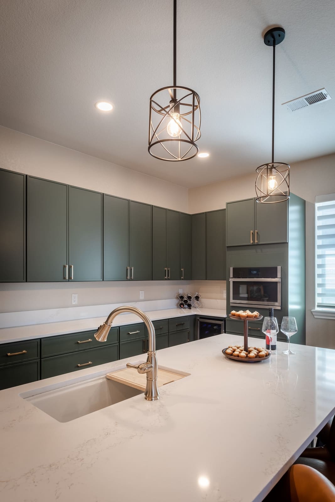 White quartz island with a brass faucet under cage pendants, sage cabinetry behind