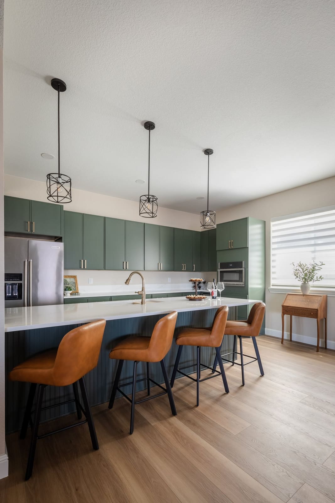 Long view of the sage kitchen island with cognac stools under cage pendants
