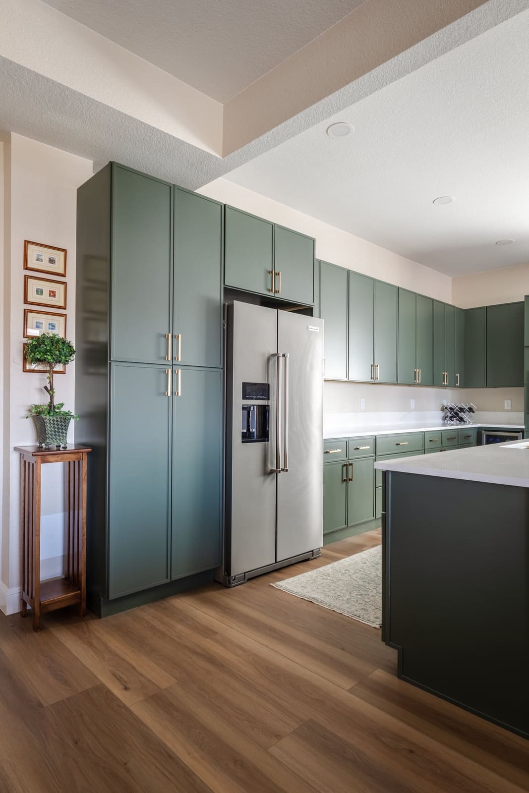 Sage pantry cabinets and stainless refrigerator beside the island