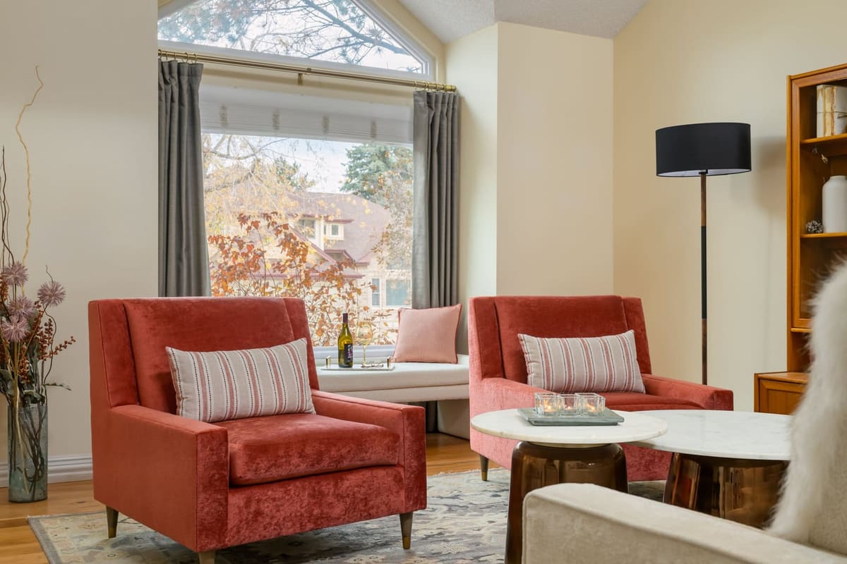Terracotta velvet chairs by a window seat with gray drapes on a brass rod and marble nesting tables