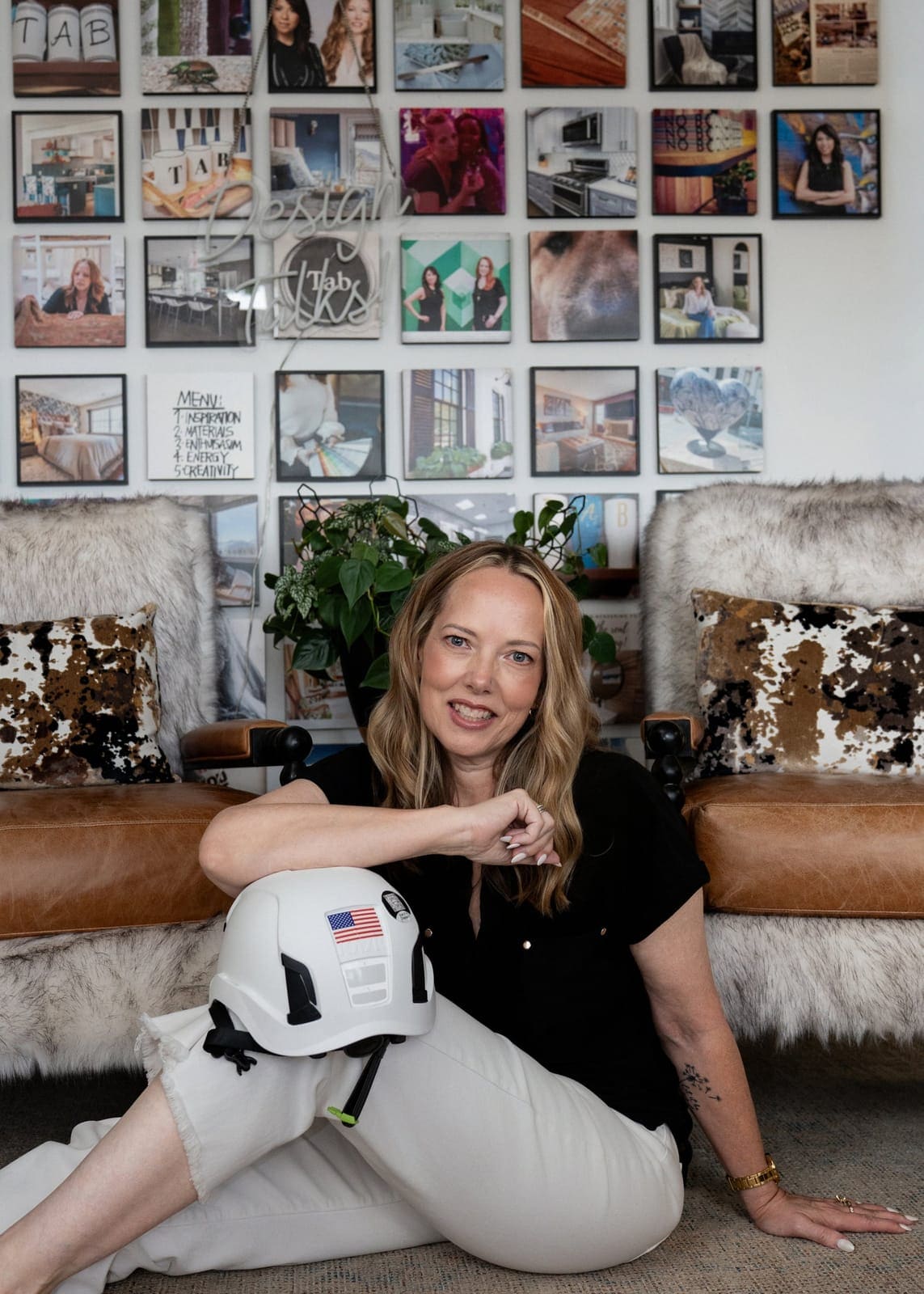 Trish Bonney seated on the studio floor with a white hard hat in front of the TAB project photo wall