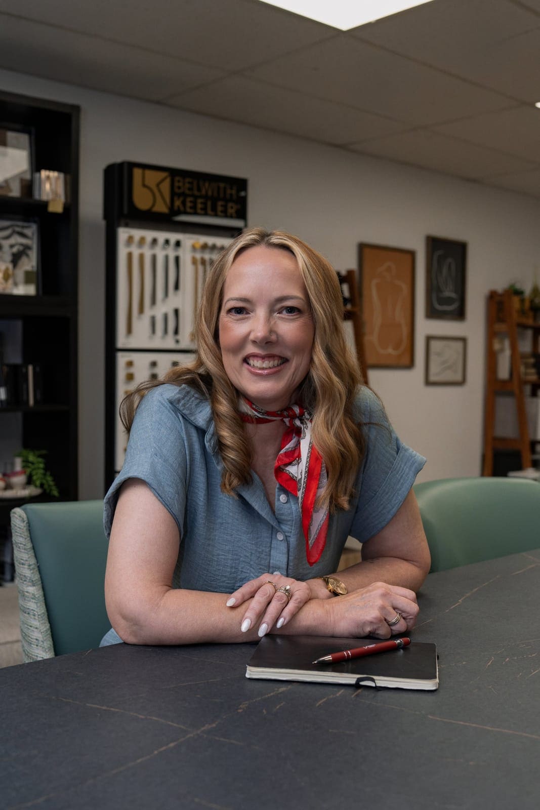 Trish Bonney in a chambray shirt and red scarf smiling at the TAB showroom table with a notebook