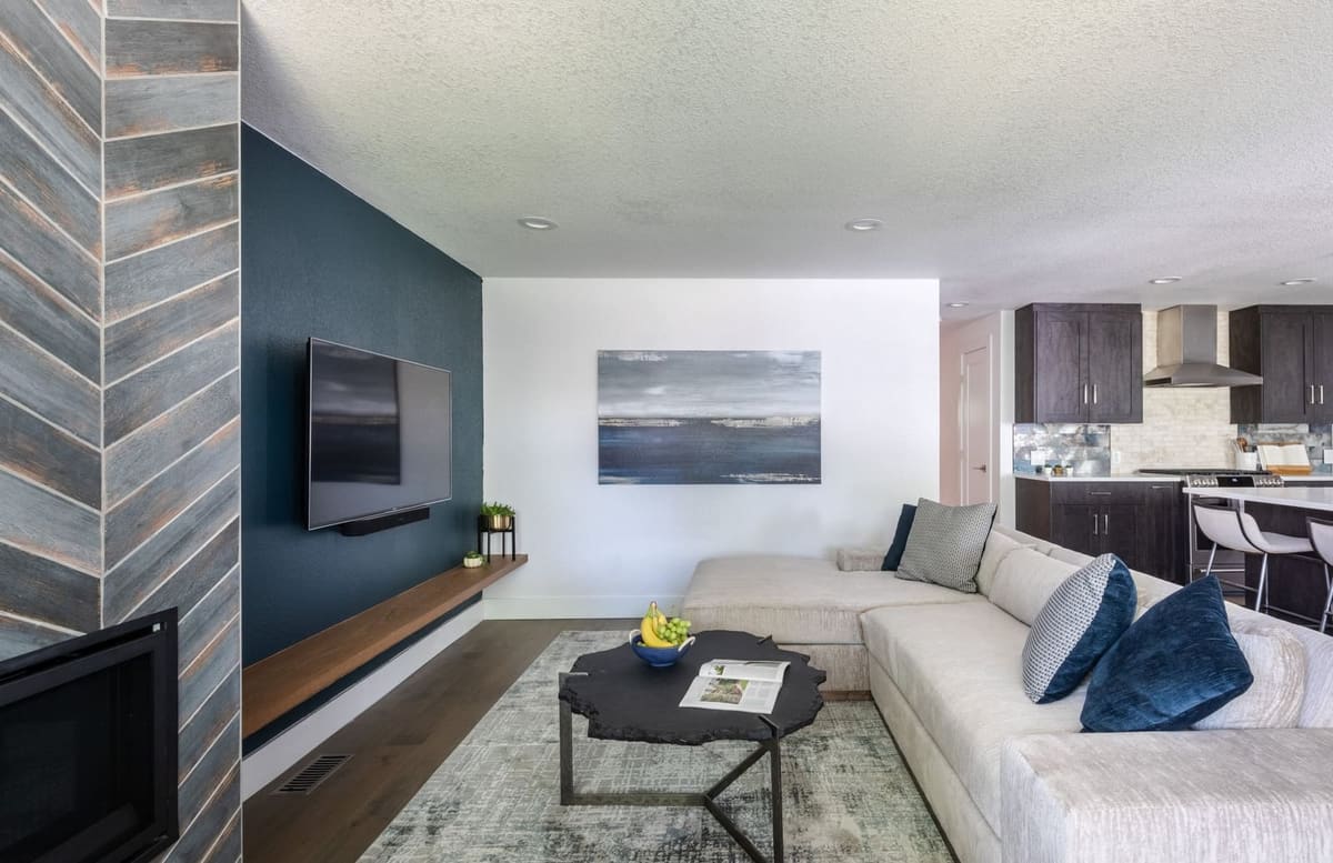 Navy accent wall with a floating walnut shelf, white sectional and chevron tile fireplace column