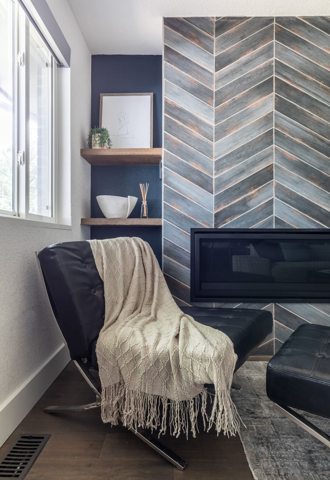 Leather lounge chair with a cream throw beside the chevron tile fireplace and floating shelves