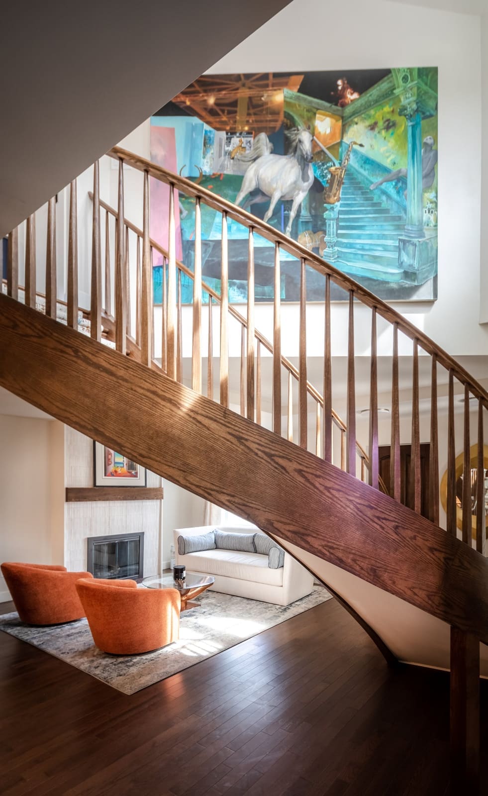 Curved staircase framing a living room with orange chairs, a colorful painting above