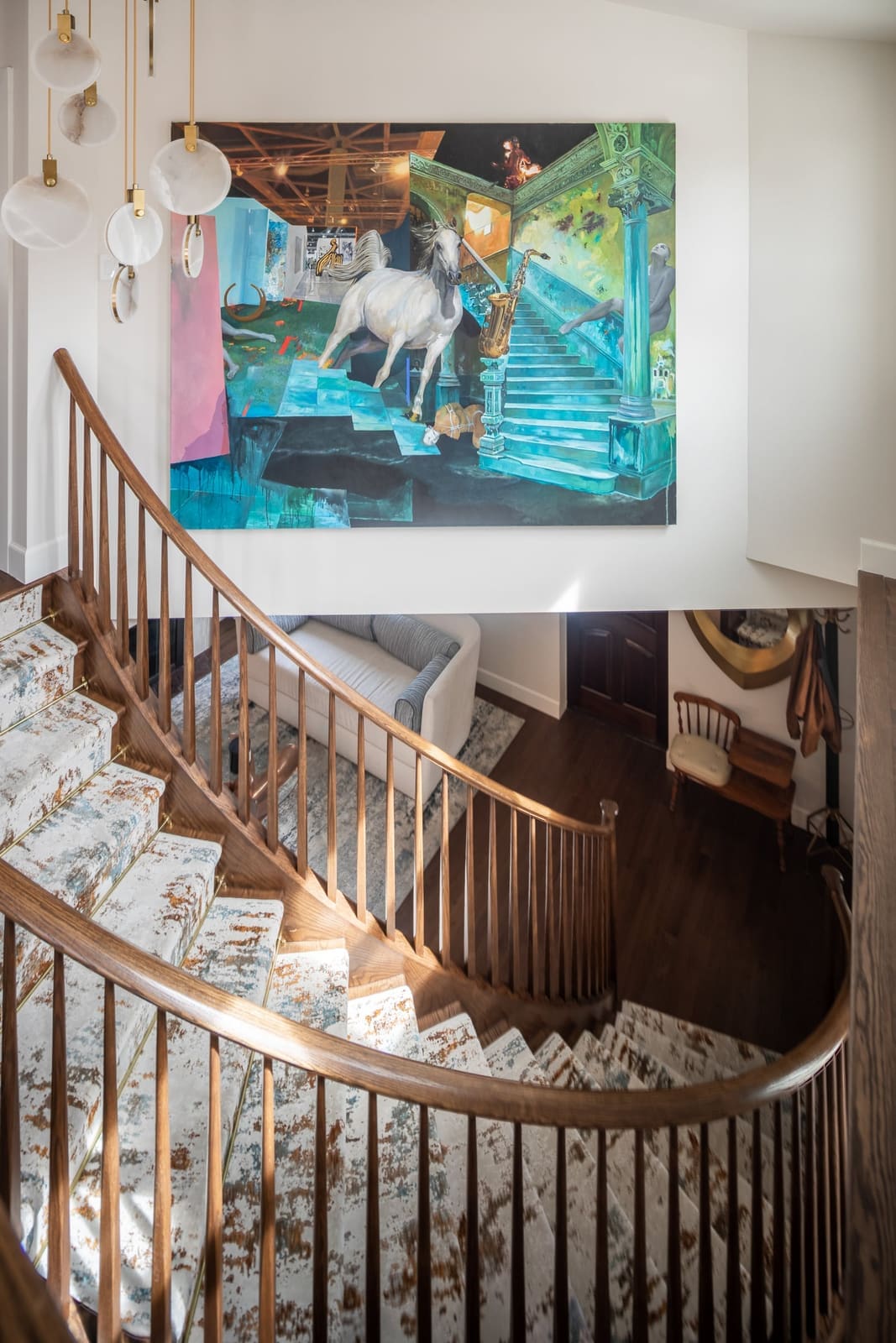 Curved staircase spiraling below a large colorful painting and a glass pendant