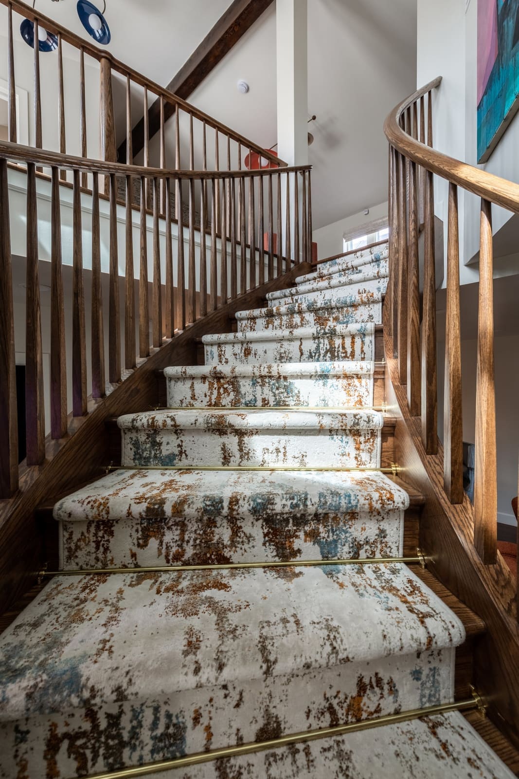 Looking up the curved wood stair with a patterned runner and slender balusters