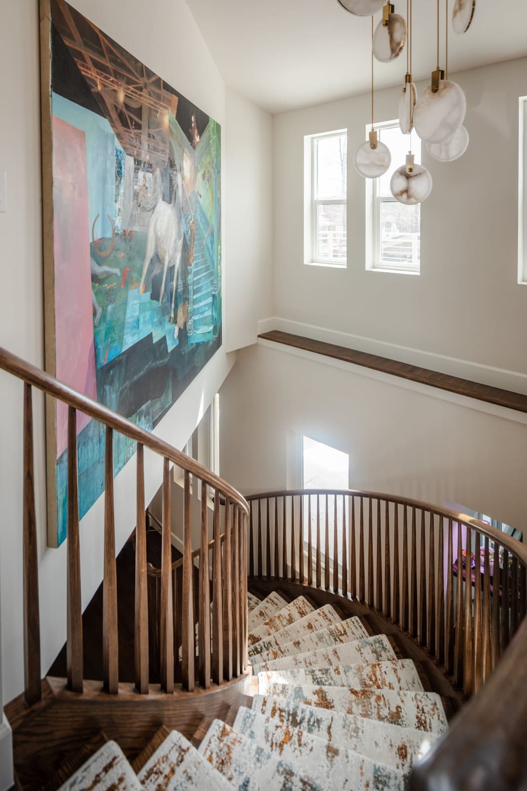 Upper landing of the curved stair beside a large painting and a cluster pendant